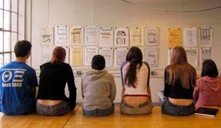 Six students sit on the edge of a table reviewing each others work.