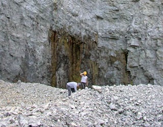 A photo of two people examining rocky ground in front of a massive cliff-face.