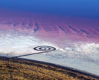 An aerial view of a spiral-shaped land art sculpture made out of mud, salt crystals, and balsalt rocks.