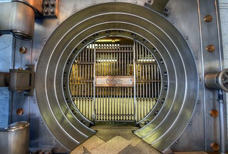 The opening of a bank vault that has metal bars surrounded by a metal circle.