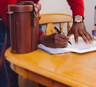 A man stands at a table and writes on a piece of paper.