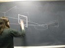 Photo of a student sketching the picture frame through which she saw the lute on the blackboard.