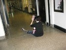 Photo of a student sitting in a hallway holding up a mirror that reflects her face and the hall behind her.