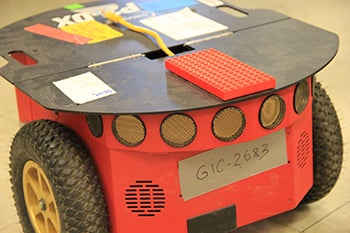 Red robot (approximately 6 inches tall with two wheels, and a flat top. A lego board is affixed to the top.