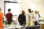 Small groups of students gather around whiteboards and work together on solving math problems.