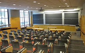 A large classroom with tiered rows of tablet desks, and large windows along one side wall.